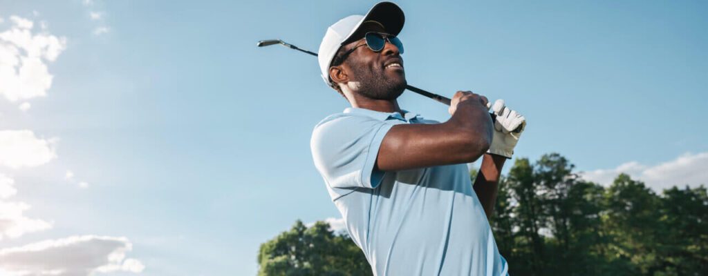 A man holding onto a golf club while wearing sunglasses.