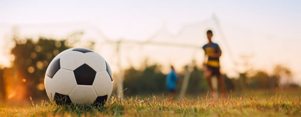 A soccer ball is in the grass with two other players.